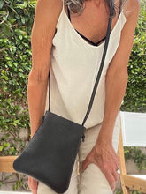 Load image into Gallery viewer, woman stands wearing x-small black leather crossbody bag. its bottom corners are rounded.  This bag is artisan made and handcrafted.
