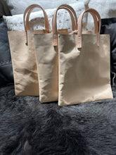 Load image into Gallery viewer, natural vegetable tanned leather bags small size, narrow-rectangular flat shape. two veg tan handles attached/sewn using belgian linen yarn. also made in distressed brown &amp; black leather and black &amp; tan suede. Retail price $195.
