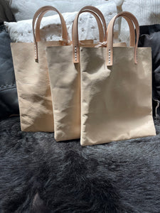 natural vegetable tanned leather bags small size, narrow-rectangular flat shape. two veg tan handles attached/sewn using belgian linen yarn. also made in distressed brown & black leather and black & tan suede. Retail price $195.