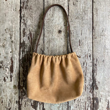 Load image into Gallery viewer, A photograph of a small tan suede bag fully gathered at the top. Its short brown strap is shoulder length. The bag’s bottom is gusseted.
