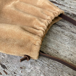Close up of a small tan suede bag fully gathered at the top its brown shoulder strap tied and knotted to both sides.