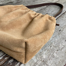 Load image into Gallery viewer, Close up of a small tan suede bag’s gusseted bottom. The bag’s top is fully gathered and has a short brown shoulder length strap.
