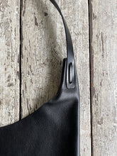 Load image into Gallery viewer, Close up of an all black leather bag focusing on the left-side shoulder strap attachment which is tied and knotted to the top of the bag. 
