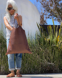 Woman holding a short handle leather bag with short v-shaped dip at center.