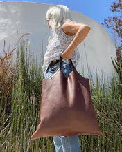 Load image into Gallery viewer, Woman holding a short handle leather bag with short v-shaped dip at center.
