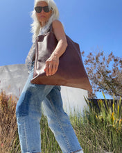 Load image into Gallery viewer, Woman wearing a large size brown leather bag with a short handle around her shoulder. The leather looks soft.
