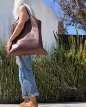 Load image into Gallery viewer, Woman wearing a large size brown leather bag with a short handle around her shoulder. The leather looks soft.
