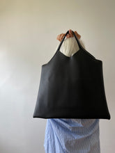 Load image into Gallery viewer, bag with short handle and a short v shaped dip at the center of the bag. the black leather used looks supple.

