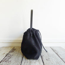 Load image into Gallery viewer, Close up of a small black suede bag fully gathered at the top and tied on one side. its black shoulder strap tied and knotted to both sides. The bag’s bottom is gusseted.
