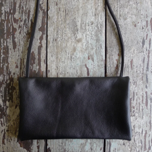 Load image into Gallery viewer, Envelope shaped black leather crossbody bag lays on a table top. The size of this bag is close to that of a standard #10 envelope.
