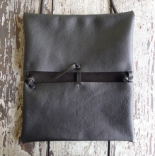 Load image into Gallery viewer, A folded envelope-style bag is open and laying flat. On the inside you can see the bag is made up of two separate pocket pouches with a tie in the center connecting and holding each pocket together. There is a cross stitch detail that attaches the tie to the bag. The envelope bag is shown in black leather.
