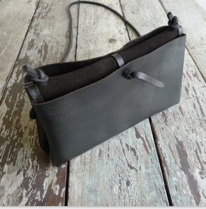 An envelope-style bag is folded inside out exposing one of the two separate pocket pouch’s and the tie that connects and holds each pocket together. Untie the knot to open. This envelope bag is shown in distressed black leather.