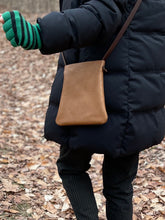 Load image into Gallery viewer, woman stands wearing x-small tan leather crossbody bag. its bottom corners are rounded.

