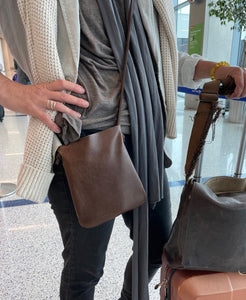 woman stands wearing x-small distressed brown leather crossbody bag. its bottom corners are rounded. This bag is artisan made and handcrafted.
