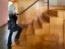 Load image into Gallery viewer, Black leather bag with three rows of wide black leather hand sewn  fringe covering 1/3 of the small-size bag starting at the top and worn by a white haired woman walking up wood stairs
