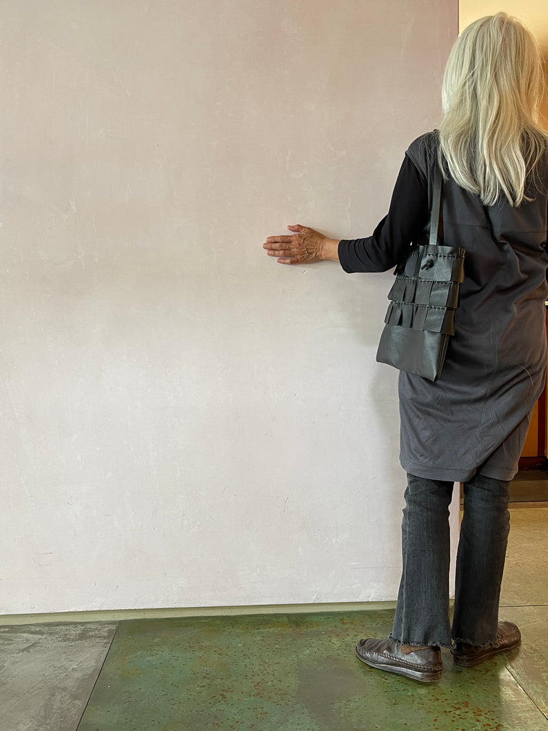 Black leather bag with three rows of wide black leather hand sewn fringe covering 1/3 of the small-size bag starting at the top and worn by a white haired woman with her back towards the viewer.