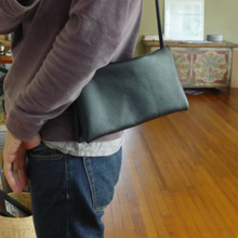 Load image into Gallery viewer, Person standing wearing an envelope shaped black leather crossbody bag. The bag is made of two separate “envelopes” its size being close to a standard #10.
