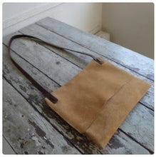 Load image into Gallery viewer, A tan suede rectangular shaped bag lays flat on a table top. Its flap is closed. The shoulder strap is tied and knotted to the top of the bag.
