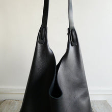 Load image into Gallery viewer, Close up of an all black leather bag focusing on the shoulder strap attachment which is tied and knotted to the top of the bag.
