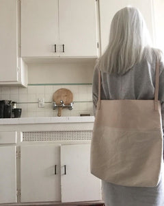 Back to the viewer, a white haired woman in kitchen wears a combination of natural denim & natural-veg tan leather bag on her back (like you would wear a backpack). This bag is artisan made and handcrafted.