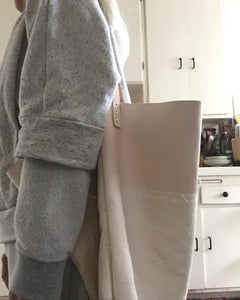 Side view of a person wearing a combination of natural denim & natural-veg tan leather bag. Two shoulder length veg tan leather straps are hand sewn using white linen yarn to the top of the bag attached on each side.This bag is artisan made and handcrafted.