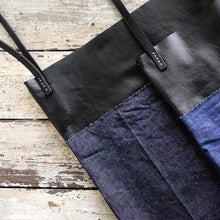 Load image into Gallery viewer, a close up two bags made from a combination of blue denim &amp; black leather material. Two shoulder length black leather straps are hand sewn to the top of the bag using grey linen yarn and are attached on each side. This bag is artisan made and handcrafted.
