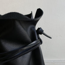 Load image into Gallery viewer, Close up detail of black leather drawstring bag strap and tie loop connection. 
