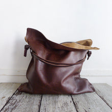 Load image into Gallery viewer, Close up of distressed brown leather bag. Drawstring style— the brown leather ties cinch in for closure. Ties are removable to wear bag to its fully extended width. Made with knotted and adjustable strap. The top of the bag is folded open exposing its suede interior. The bags leather looks soft and supple.
