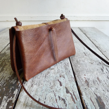 Load image into Gallery viewer, An envelope-style bag is folded inside out exposing one of the two separate pocket pouch’s and the tie that connects and holds each pocket together. Untie the knot to open. This envelope bag is shown in distressed brown leather.
