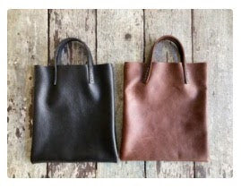 Black and brown leather bags small size, narrow-rectangular flat shape. two veg tan handles attached/sewn using belgian linen yarn. also made in natural vegetable tanned leather and black & tan suede. Retail price $195.